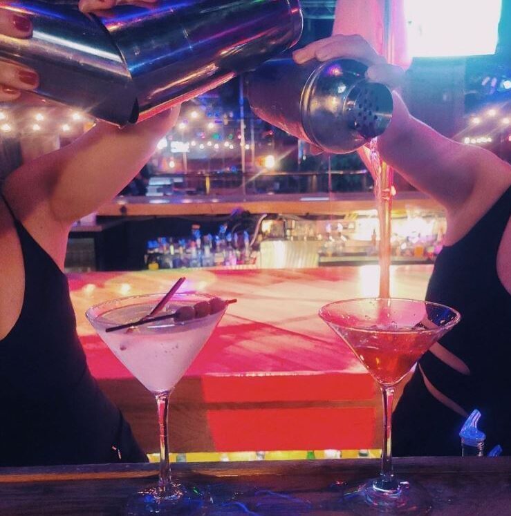 Two female bartenders pouring cocktails in martini glasses.